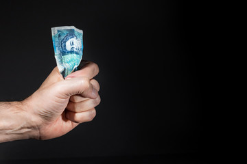 A male hand holding a five pound banknote on his fist, isolated over black.