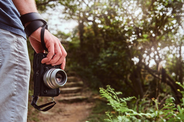 Fototapeta premium Man is holding camera in his hand while walking by the path throw the green mountains