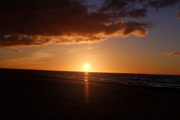 Fototapeta na wymiar Dark sunset in with sun, sea, clouds and orange tones