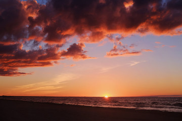 Fototapeta na wymiar Setting sun, calm sea and colourful clouds at the seaside on a dusk time