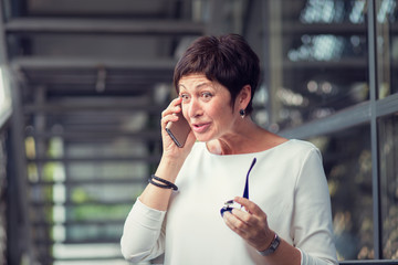 A mature woman talking at mobile phone stunned by what she hears,