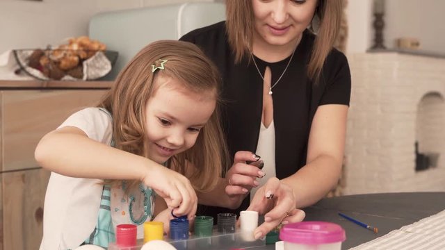 Young mother and her cute little daughter are opening a boxes with paints cause they are goig to paint eggs on Easter.