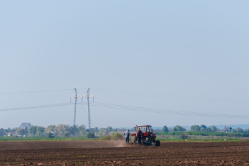 a red tractor and workers in the field of land preparation for planting