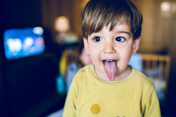 Portrait of a little boy in yellow showing his tongue in dark room at home