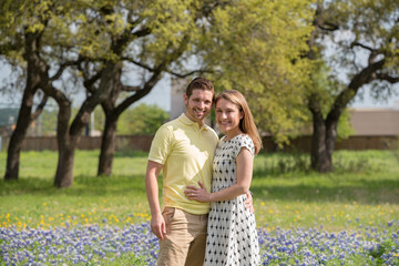 Fototapeta premium Young Millennial Couple Standing During Spring in a Field of Blue Bonnets