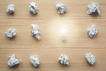 Many crumpled white paper balls with one light bulb between them. Concept of think different, think out of the box, leadership.