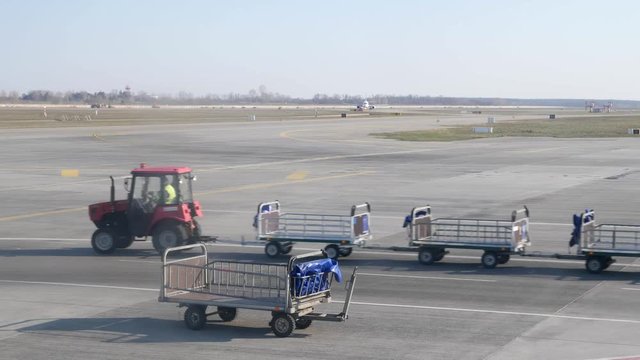 Empty baggage cart in the aiport. Tracktor with emty baggage carts passing by the plane.