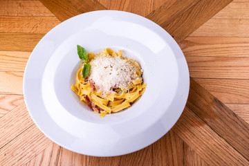 Classic Carbonara pasta, spaghetti with pancetta, bacon, egg, parmesan cheese and green arugula on wooden table.