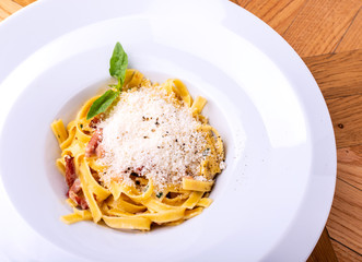 Classic Carbonara pasta, spaghetti with pancetta, bacon, egg, parmesan cheese and green arugula on wooden table.