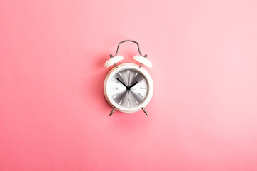Retro white and silver alarm clock on a pink background. Time concept, top view, flat lay 