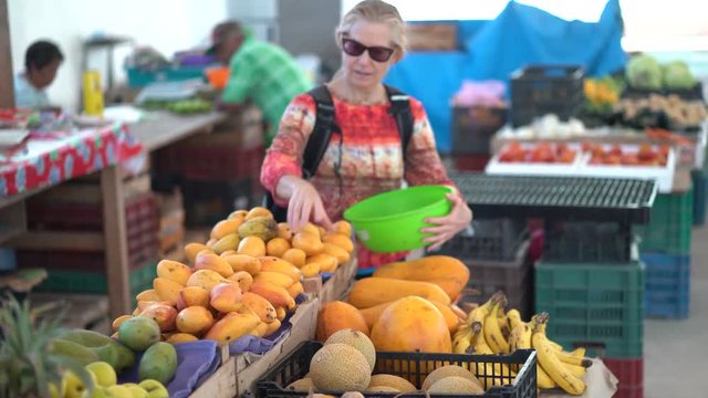 Mature woman picking mangoes at a farmers market and smelling and having her son smell for freshness.