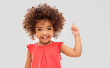 idea, warning and childhood concept - happy little african american girl pointing finger up over...