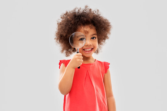 investigation, discovery and vision concept - happy little african american girl looking through magnifying glass over grey background - Powered by Adobe