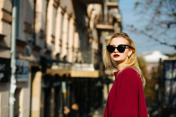 Gorgeous woman wearing sweater and sunglasses posing at the city. Empty space