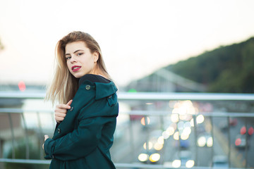 Adorable young woman wearing green coat posing at the bridge with lights. Space for text