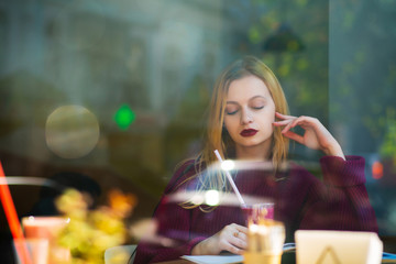 Attractive blonde model spending time in the restaurant with a cup of smoothies. Shot through window glass. Empty space