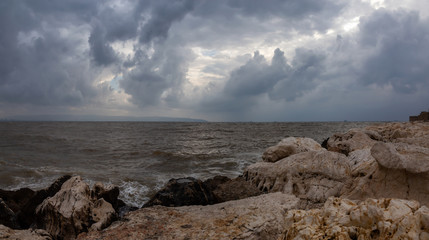 Beautiful view on the rocky and muddy coast near the Old City of Akko during a cloudy and sunny day. Taken in Acre, Israel.
