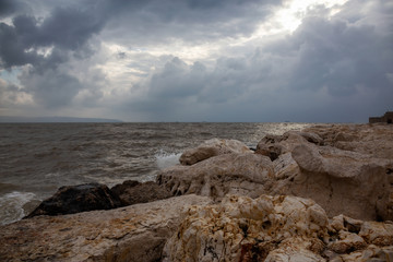 Beautiful view on the rocky and muddy coast near the Old City of Akko during a cloudy and sunny day. Taken in Acre, Israel.