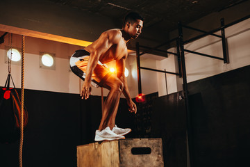 Fit young man doing a box jump exercise. Sports man doing a box squat at the gym