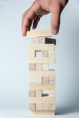 Male hand puts a cube on the tower of wooden cubes, as a symbol of support, teamwork and business development. Vertical frame