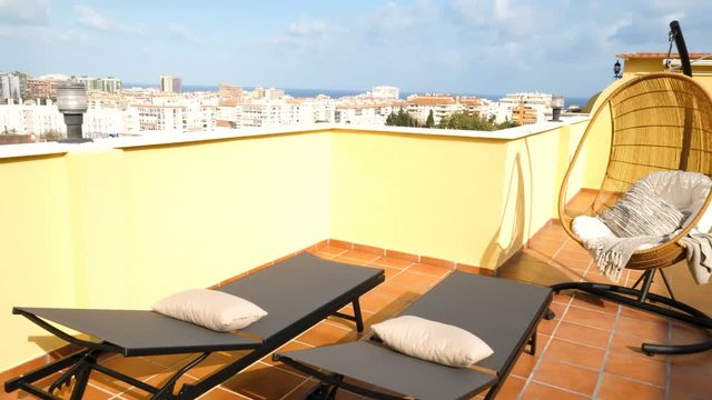 Hanging chair and sun beds in a sunny terrace of a relaxing summer holiday destination with sea view.
