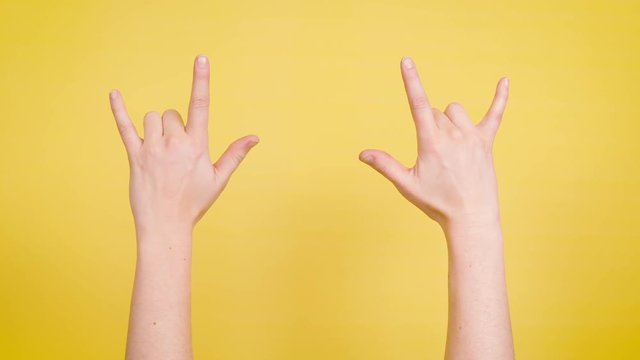 Hands make rock symbol on yellow backdrop.