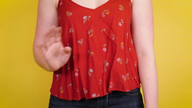 Woman waves on yellow backdrop.