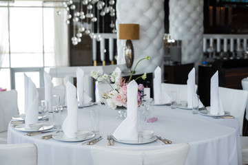 closeup white napkins stand in  white plates on served table in the restaurant. clean white dishes layout on a white tablecloth