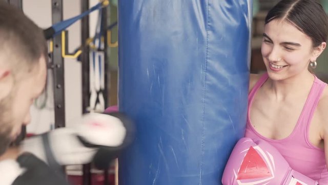 Young attractive woman and man in a boxing gloves is training boxing in a gym. They are working on their boxing techniques with a punching bag.