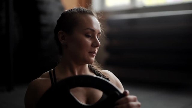 Athletic beautiful woman close-up on face doing twisting in slow motion in the gym, holding in hands the weight from the barbell. Sexy girl trains abdominal muscles on the functional crossfit training