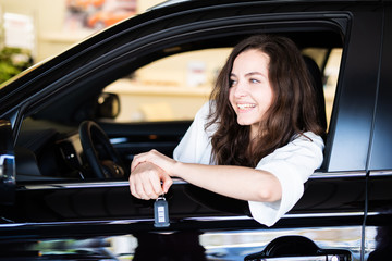 Junge Frau sitzt freudig lachend in einem neuen Auto in einem Autohaus 