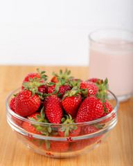 Fresh strawberry in a bowl and glass of milk on wooden background.