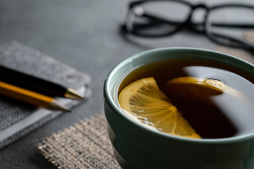 Black tea with lemon slices on a napkin of burlap with notepad pen, a pencil and glasses