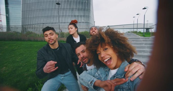 Slow motion of group of young friends of different ethnicities are having fun and making a selfie together with cellular phone in a city center with skyscrapers