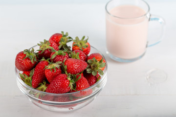 Fresh strawberry in a bowl and glass of milk on wooden background.