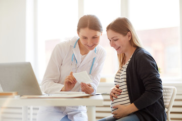 Portrait of smiling female obstetrician consulting pregnant woman in doctors office, copy space
