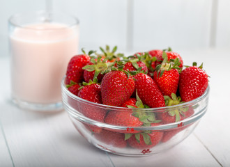 Fresh strawberry in a bowl and glass of milk on wooden background.
