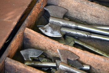 Shiny handmade middle ages axes in a wooden box on a traditional market.