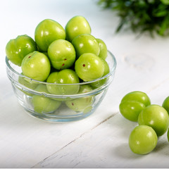 Green plums in glass bowl on wooden table 