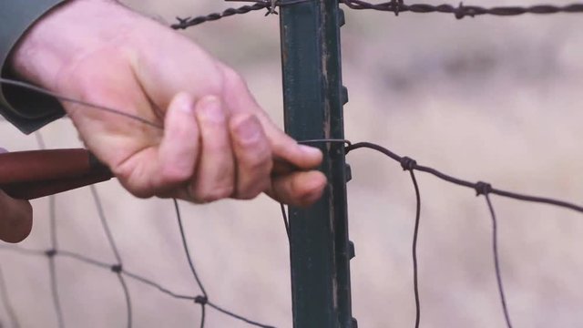 Close up detail shot of male hands twisting new wire on a farm land fence in West, Texas, 60 fps, 4K.