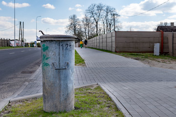 Obraz premium Old trash bin standing on the sidewalk by the road in the city. Metal bucket for municipal waste.