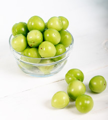 Green plums in glass bowl on wooden table 