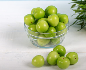 Green plums in glass bowl on wooden table 