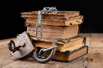 Old books bound by a new shiny chain with an old padlock. Forbidden old works artists on a wooden table.