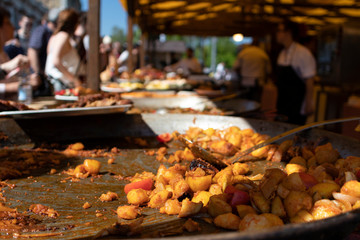 Street food festival on a bright sunny day in Budapest, Hungary. A giant pot with traditional local chicken stew, half empty. Man serves customers in the background, out of focus.