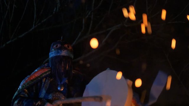 The shaman hits the drum sitting by the fire.