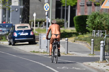 An almost naked elderly man with gray hair rides a bicycle on a warm and sunny spring day in Berlin...