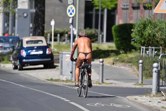 An almost naked elderly man with gray hair rides a bicycle on a warm and sunny spring day in Berlin Germany