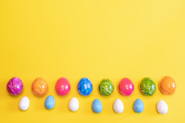 A lot of colorful Easter eggs on a yellow background. Top view, minimal Easter concept. Happy Easter card  with free, empty space.