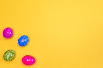Four colored Easter eggs on a yellow background. Top view. Happy Easter card  with free, empty space. Minimal Easter concept.
